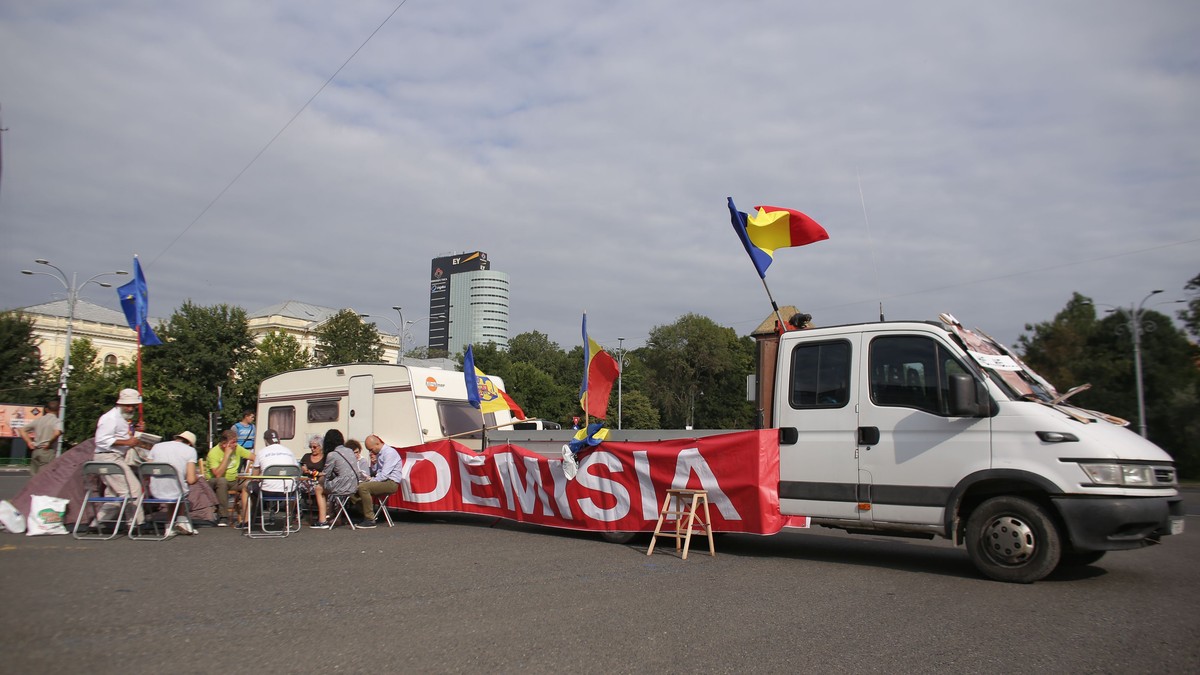 Primii manifestanți au ajuns cu rulota în Piața Victoriei. Fotografie din Piața Victoriei, cu o rulotă și un banner pe care scrie DEMISIA