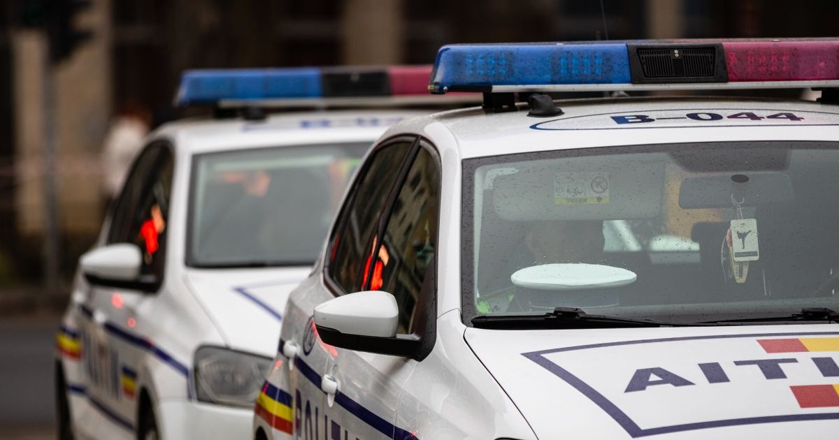 Două mașini de Poliție, una în fața celeilalte, în prim plan, pe o stradă