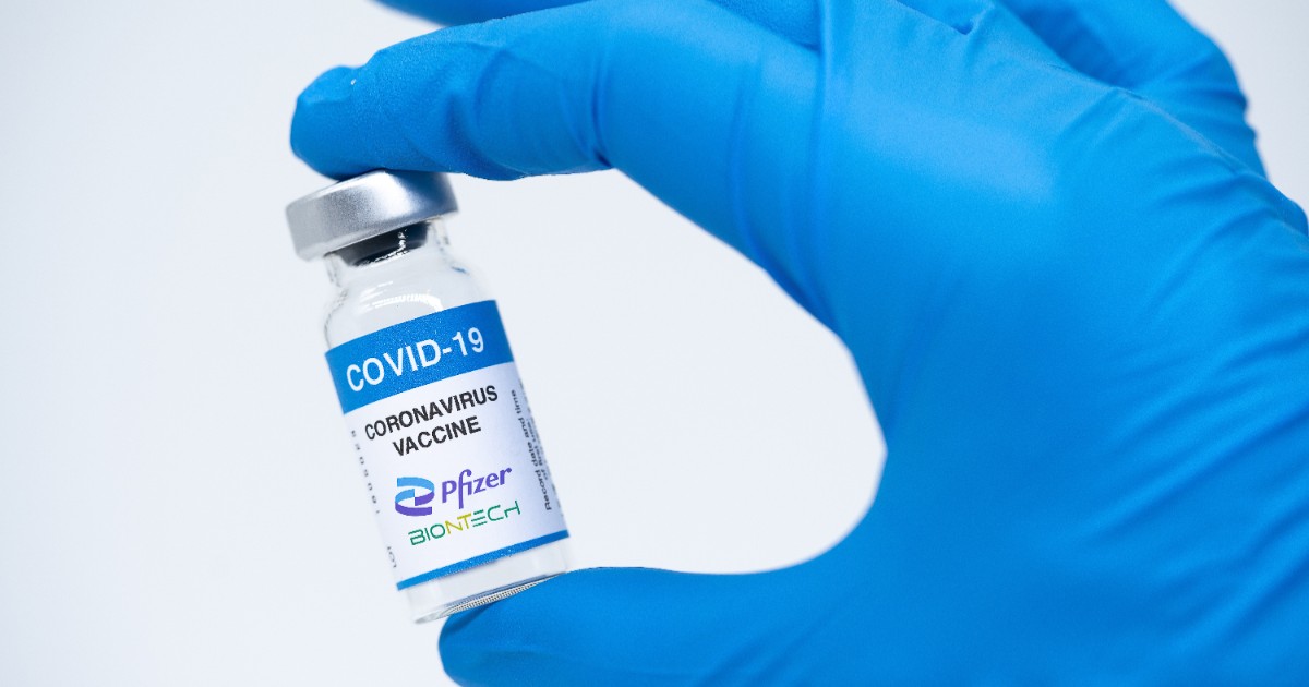 O asistentă ține în mână o doză de vaccin anti-COVID de la Pfizer și poartă o mânușă albastră