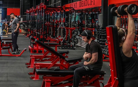 Imagine dintr-o sală de fitness, cu mai mulți oameni antrenându-se la diverse aparate