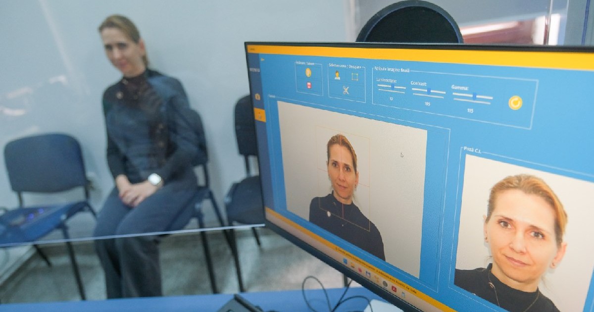 O femeie blonda, îmbrăcată în bleumarin, stă pe un scaun, pentru a i se face o fotografie pentru cartea de identitate electronica