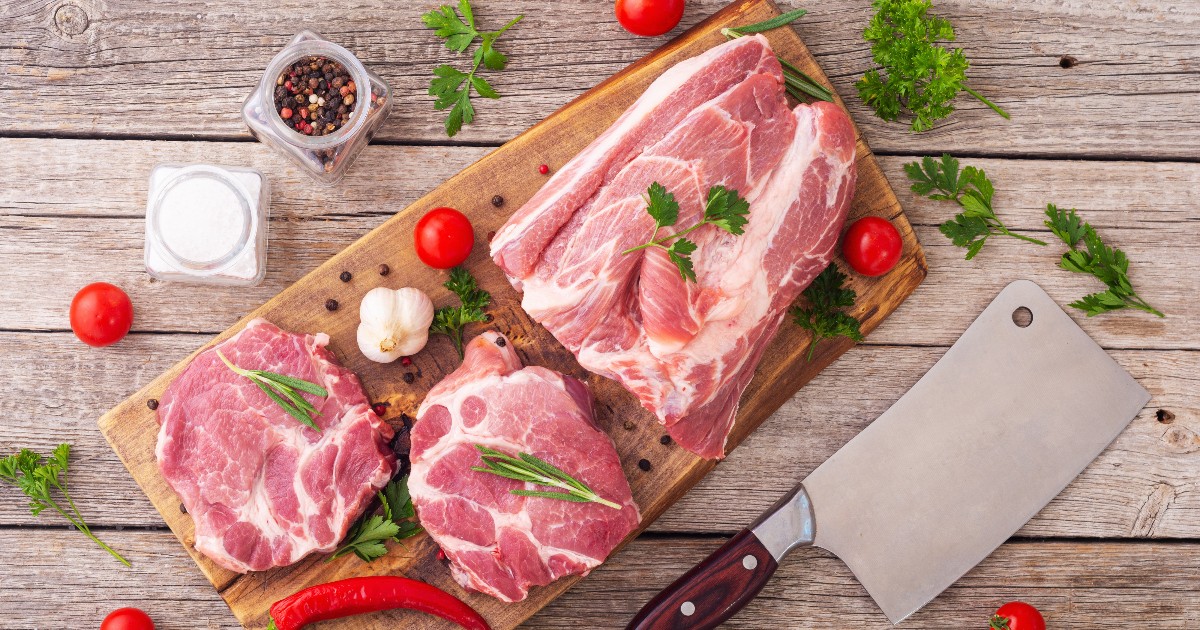 ChatGPT said: În imagine se află bucăți de carne de porc crudă, așezate pe un tocător din lemn. Carnea este însoțită de diferite ingrediente folosite la gătit: roșii cherry, ardei iute roșu, usturoi, boabe de piper și diverse verdețuri (pătrunjel, rozmarin). În partea dreaptă, pe tocător, se află un satâr mare cu mâner din lemn.