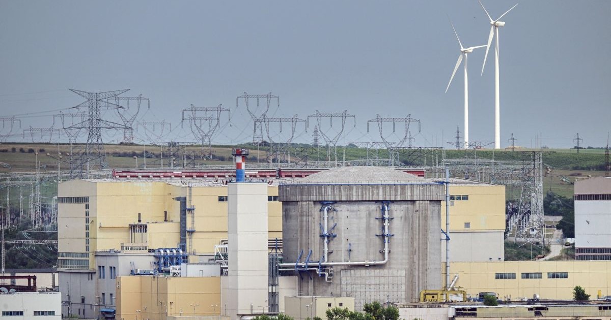 Centrala Nucleară de la Cernavodă, cu clădirile din complex, iar pe fundal eoliene de culoare albă și stâlpi de înaltă tensiune