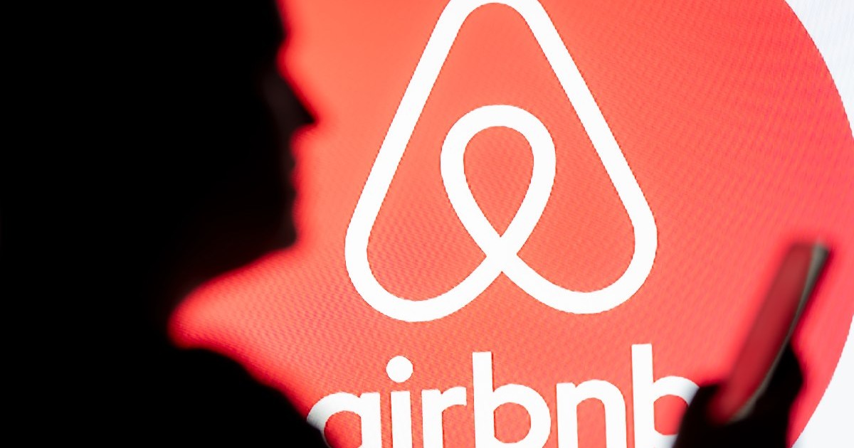 o femeie se uită la un smartphone cu logo-ul Airbnb afișat în fundal