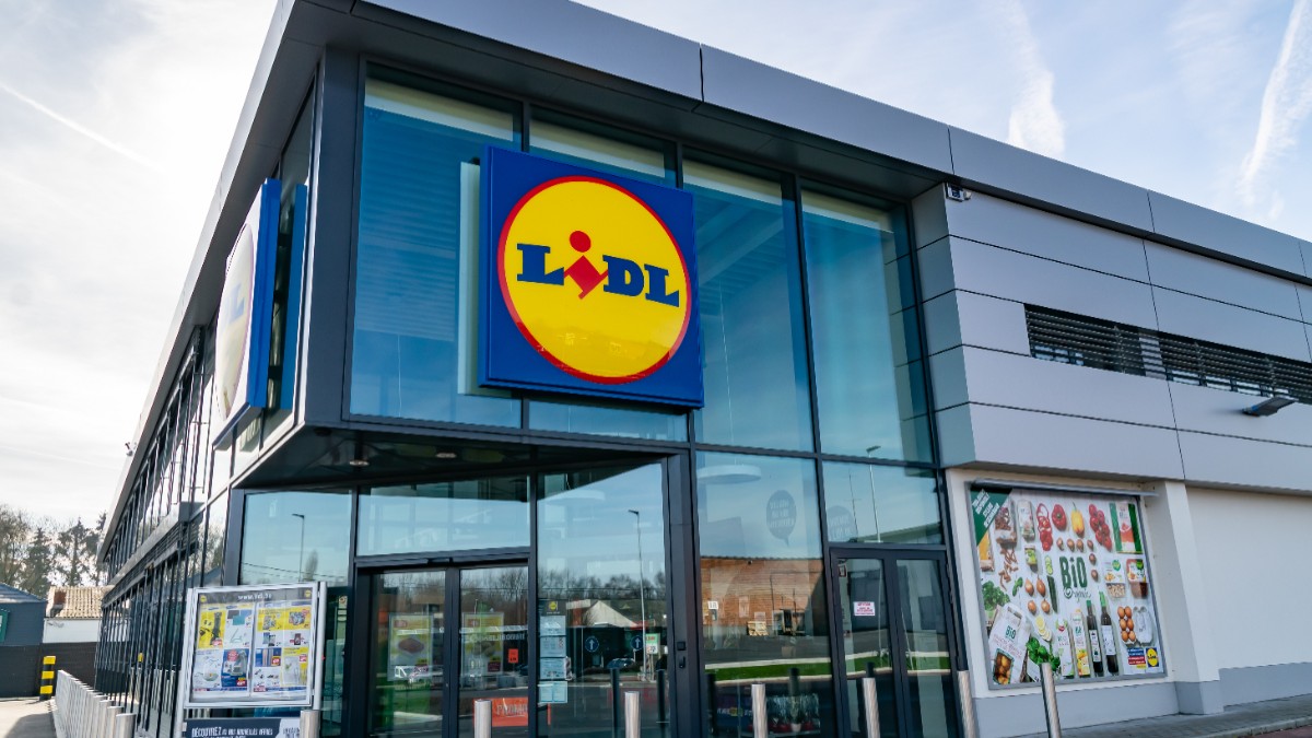 Fațada unui magazin Lidl, pe care este amplasată sigla mare, circulară și multicoloră a retailerului, deasupra ușilor de la intrare.