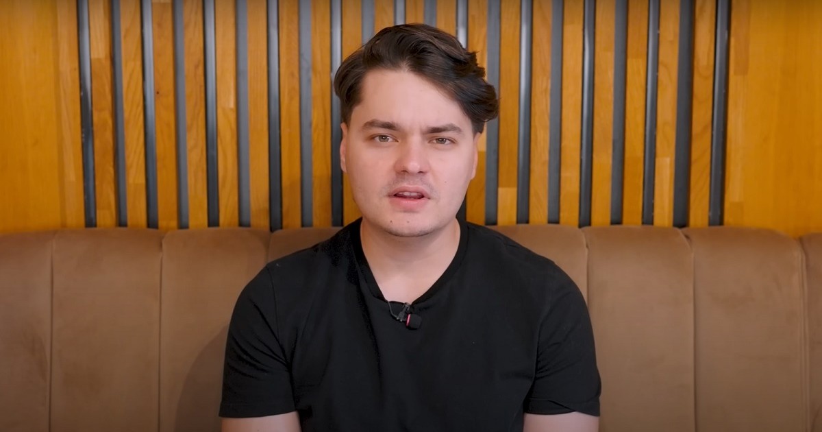 Selly este așezat pe o canapea maro, îmbrăcat într-un tricou negru