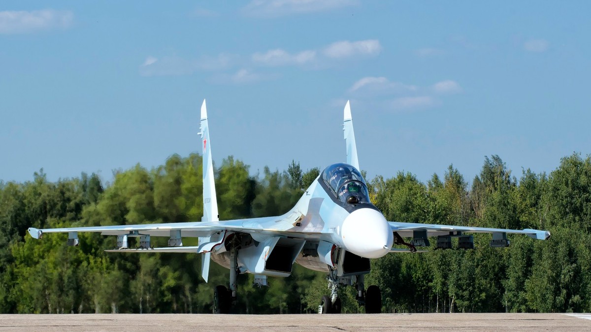avion de vânătoare rus Suhoi Su-30, de culoare albastru-alb, se pregateste sa aterizeze pe un aerodrom inconjurat de o padure