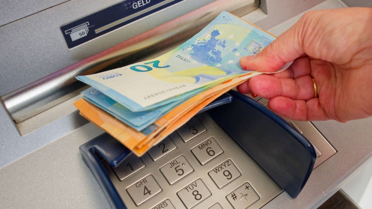 Bancnote de euro, de 20 și 50 de euro, ținute într-o mână, în fanta de retragere a unui bancomat