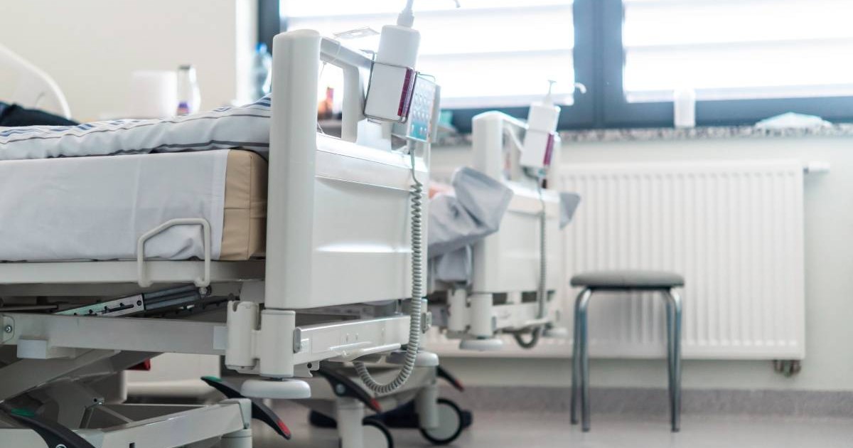 Două paturi de spital într-un salon ATI, așternuturile puse pe paturi sunt albe, fiecare pat este dotat cu dezinfectant