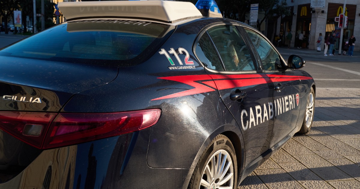 Imaginea prezintă din unghi spate-lateral o mașină de poliție a Carabinierilor italieni, un model Alfa Romeo Giulia de culoare închisă cu dungi roșii, inscripționată cu numărul de urgență 112 și parcată pe o stradă urbană.