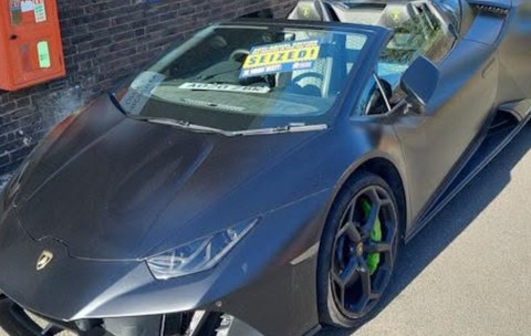 Lamborghini Huracán negru mat, care are lipit pe parbriz un afiș galben cu inscripția „SEIZED!”.