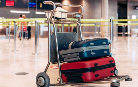 Un cărucior metalic de bagaje aflat într-un terminal de aeroport, încărcat cu două valize și o pălărie