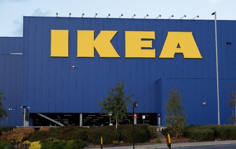 Un magazin Ikea, pereții sunt colorați cu albastru, iar literele care formează scrisul sunt galbene. În fața magazinului sunt un gard viu verde și o parcare goală