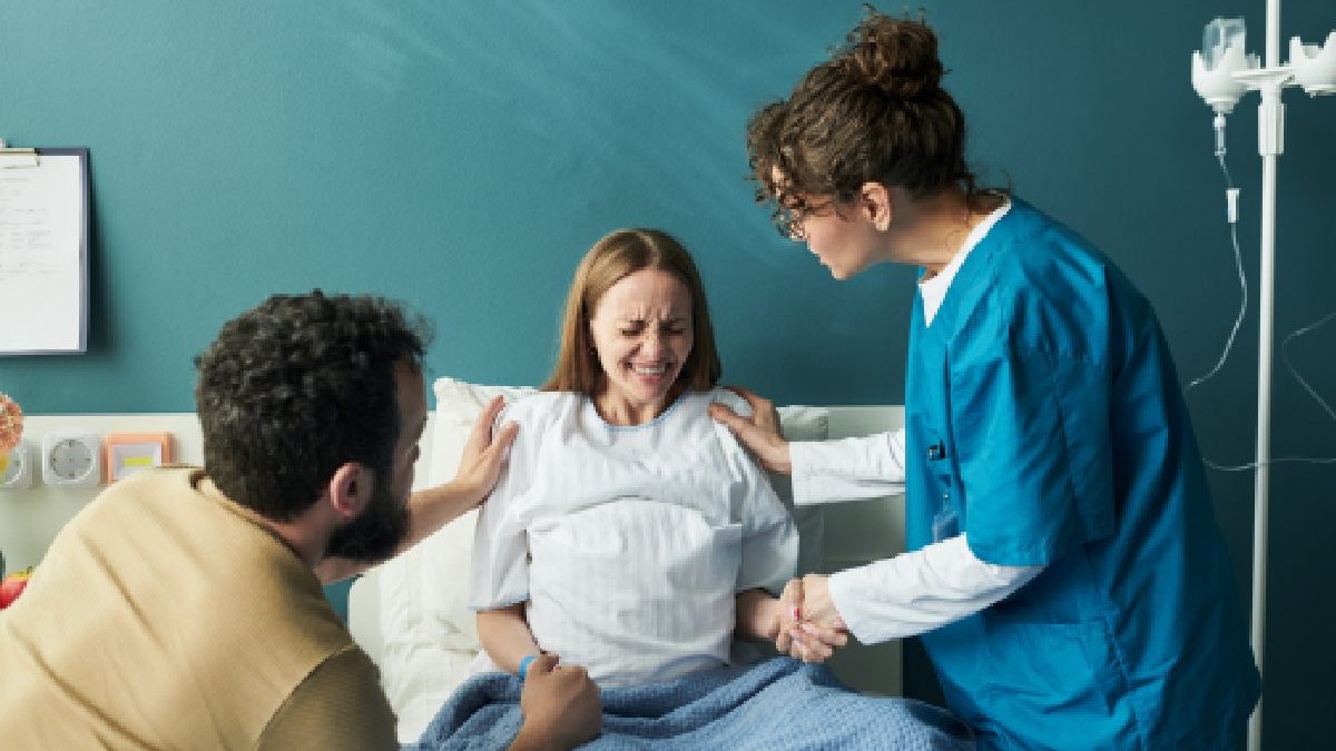 O femeie gravidă stă în pat, langa ea e partenerul si medicul. Studenta care nu stia ca e gravida a aflat ca va naste in 30 de minute