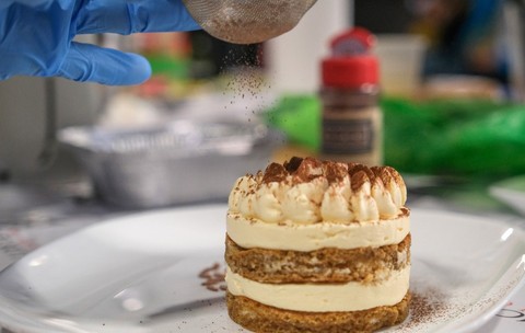 Tiramisu World Cup, un tiramisu construit sub forma de rotund, pe o farfurie. O persoană pune praf de cacao peste el