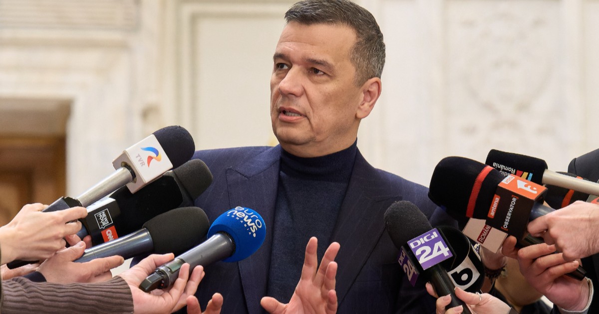 Sorin Grindeanu îmbrăcat în sacou bleumarin și maletă închisă la culoare, vorbind și gesticulând în fața jurnaliștilor.