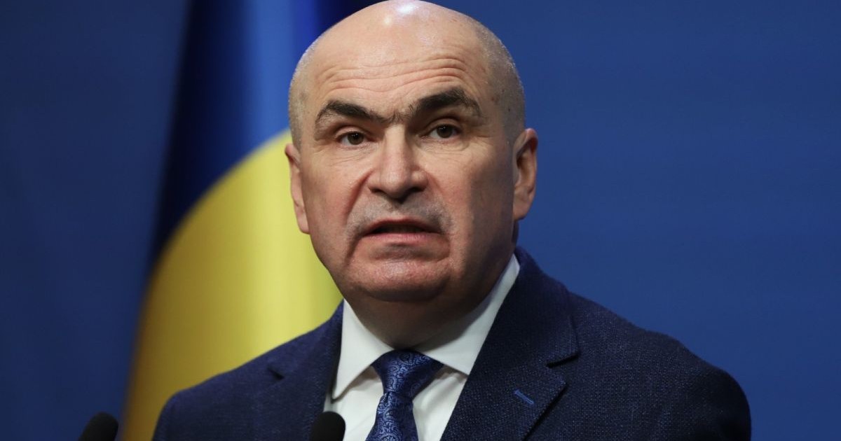 Premierul interimar Ilie Bolojan, cu steagul României în spate, la Guvern, 6 mai 2026