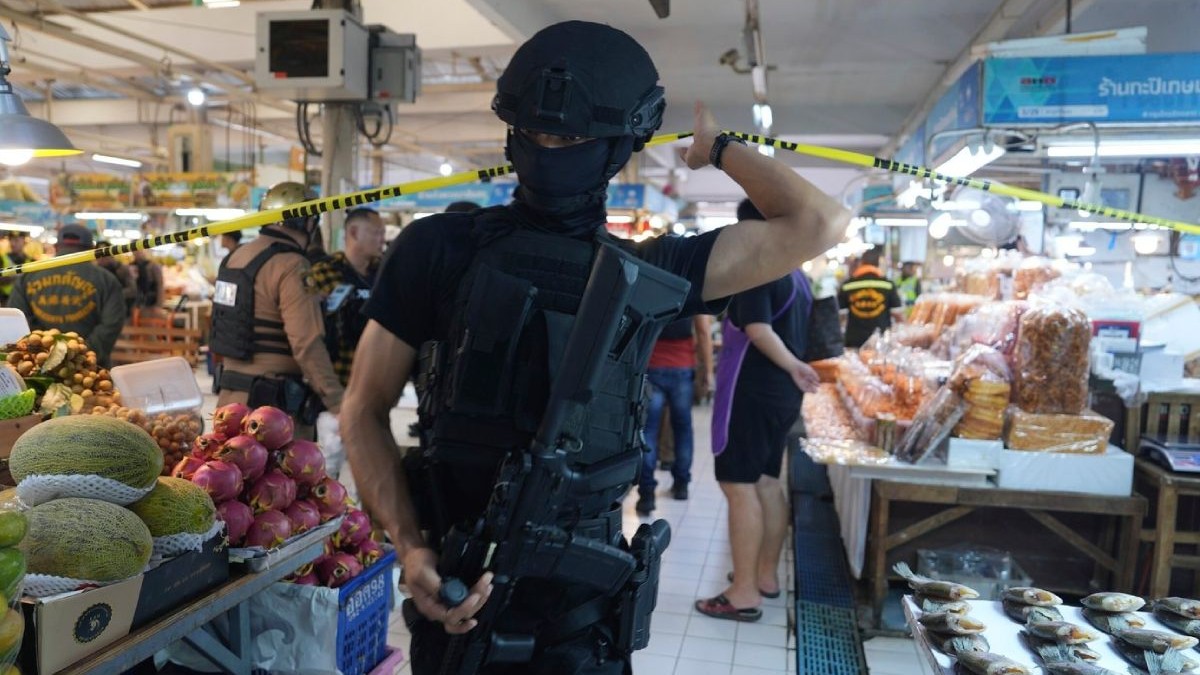 Mascați care trec o bandă de politie după un atac armat intr-o piață din Bangkok, se vad tarabe cu fructe si legume si alti oameni in fundal, 28 iulie 2025