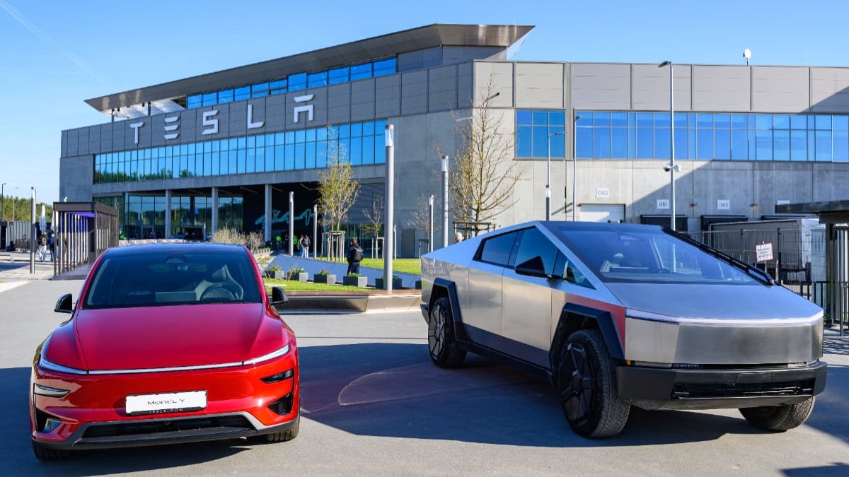 Un Tesla Cybertruck argintiu și un model Tesla roșu sunt expuse în fața unei clădiri moderne marcate cu logo-ul companiei Tesla.