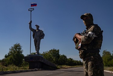 Un militar rus care stă de pază pe drum în fața monumentului oțelului cu steagul național rus la intrarea în orașul Mariupol. Foto: EPA