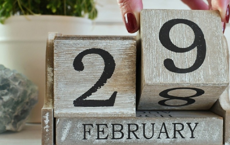 Calendar din lemn care arată data de 29 februarie, cu o mână ce mută un bloc de la 28 la 29.