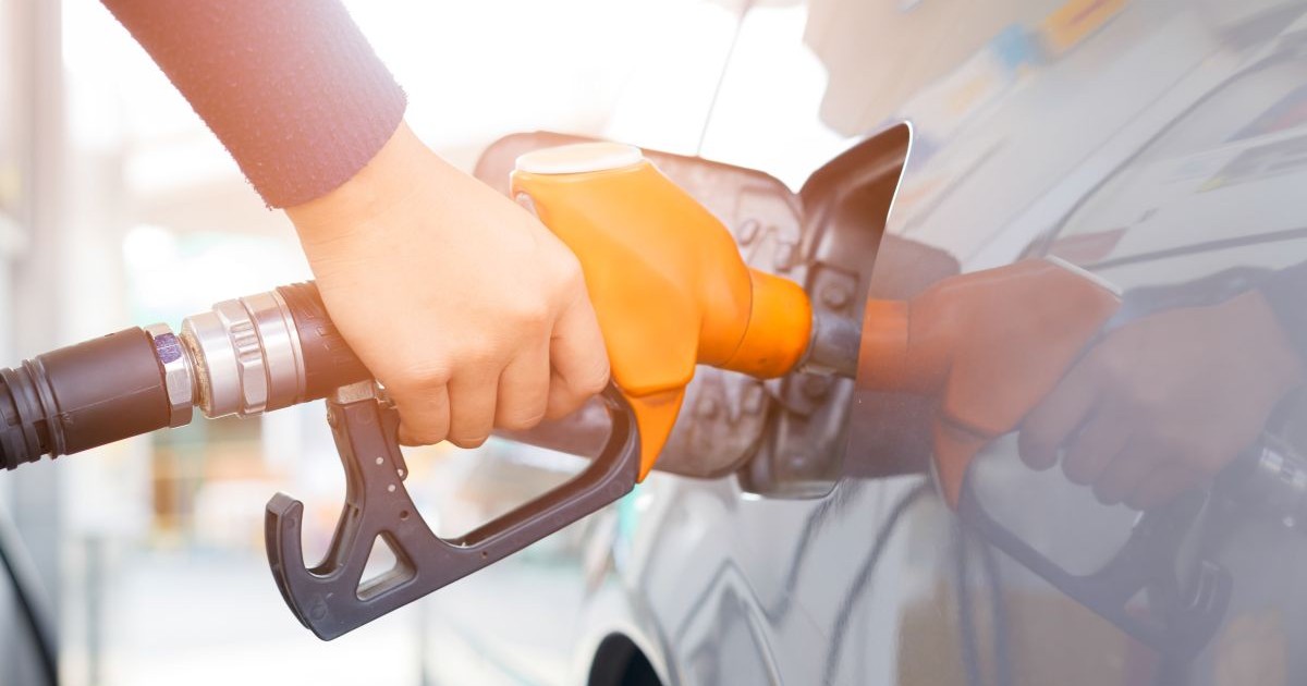 Un bărbat ține în mână o pompă portocalie și alimentează cu carburanți o mașină gri, în Thailanda