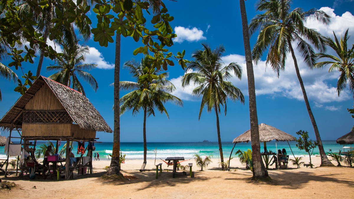 Plajă tropicală în Palawan, Filipine, cu nisip alb, palmieri, bungalouri tradiționale și apă turcoaz