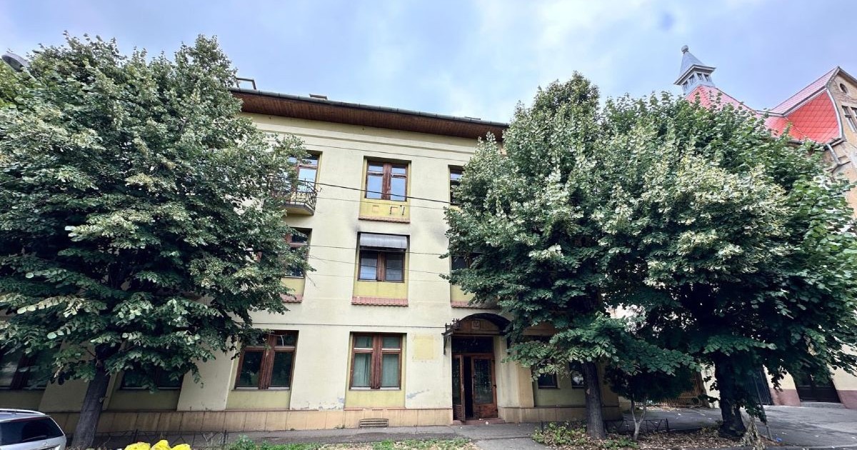 O cladire in zona Gării de Nord, marginita de doi copaci verzi, mari, saci de gunoi galbeni in fata , pe iarba