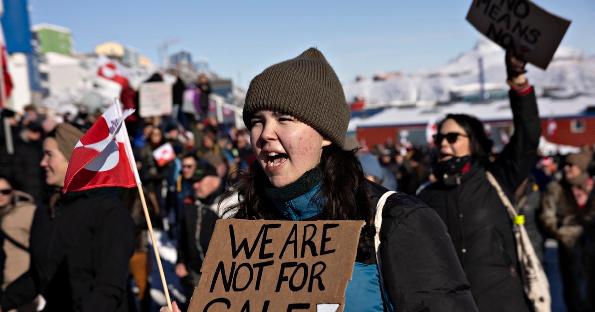 Tânără din Groenlanda care participă la un protest și care ține în mâini un panou din carton pe care scrie „Nu suntem de vânzare”