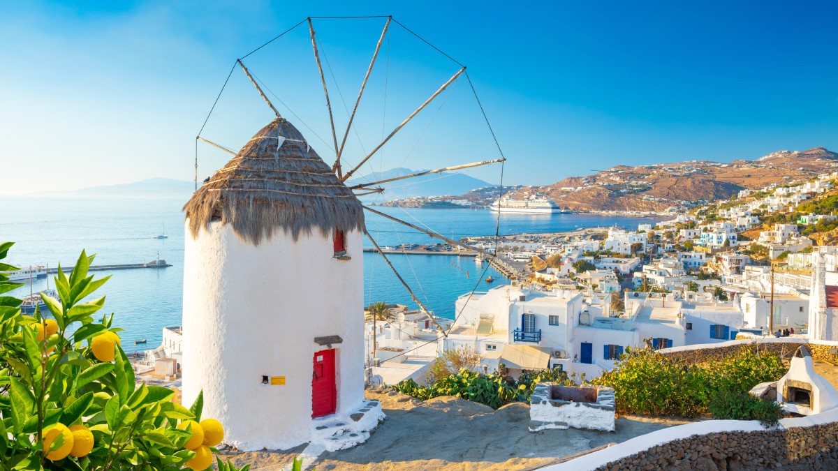 Peisaj din Mykonos, Grecia. O căsuță cu o elice în fata ei. În fundal se văd mai multe plaje și apa