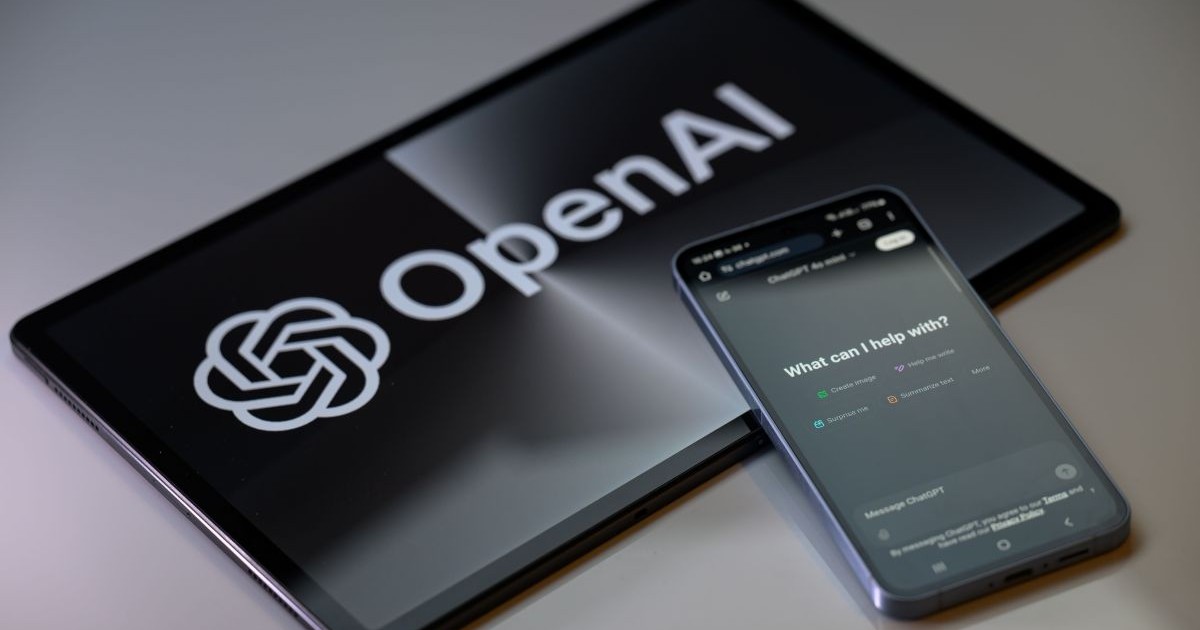 Aplicația ChatGPT, deschisă pe un telefon care stă rezemat pe o tabletă pe al cărui ecran e expus logo-ul companiei Open AI.