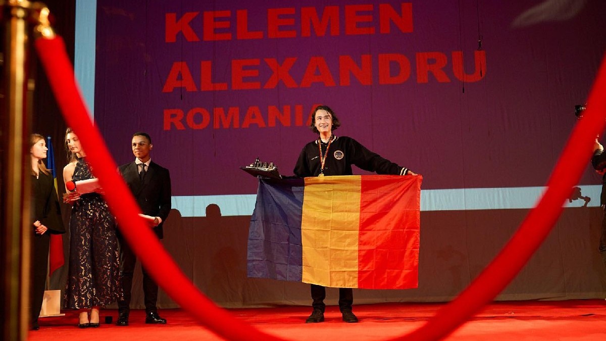 Un tânăr îmbrăcat în negru, cu o medalie la gat, tine steagul României în mâini, la Olimpiada Internationala de Astronomie, 2025