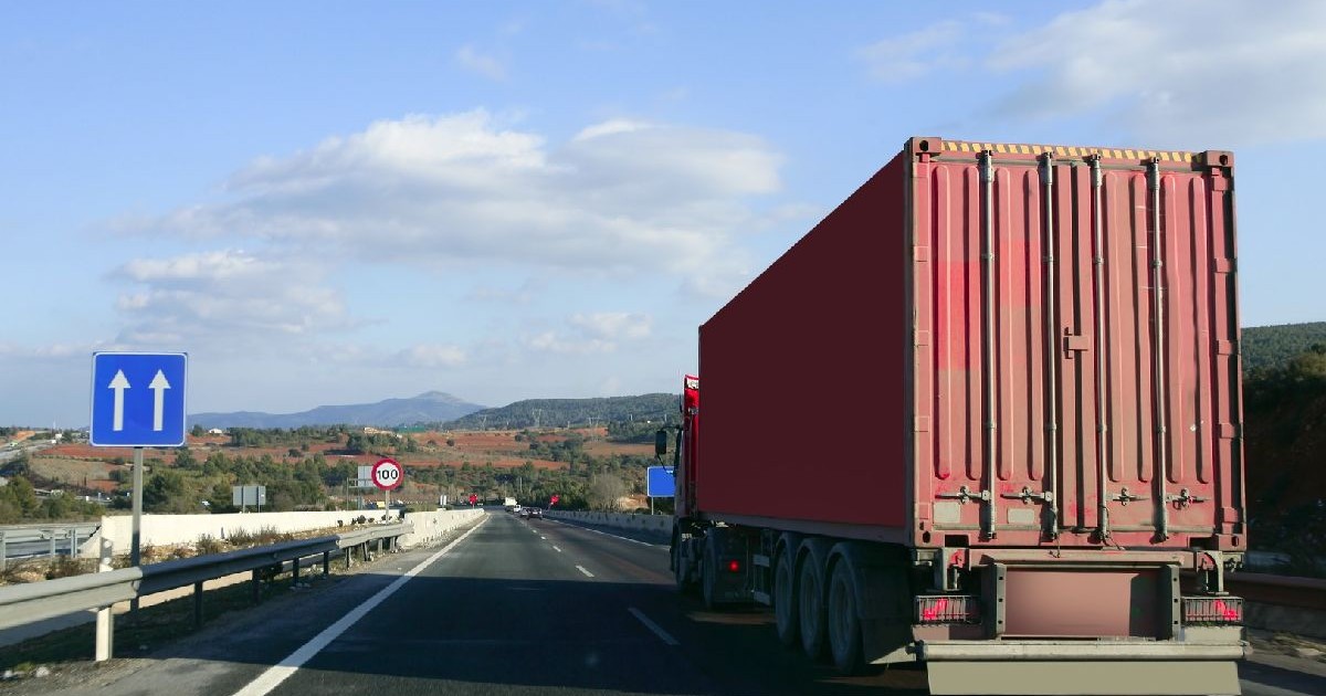 Fotografie cu un camion roșu pe o autostradă, cer albastru cu nori, peisaj rural și indicatoare de o parte și de alta a drumului.