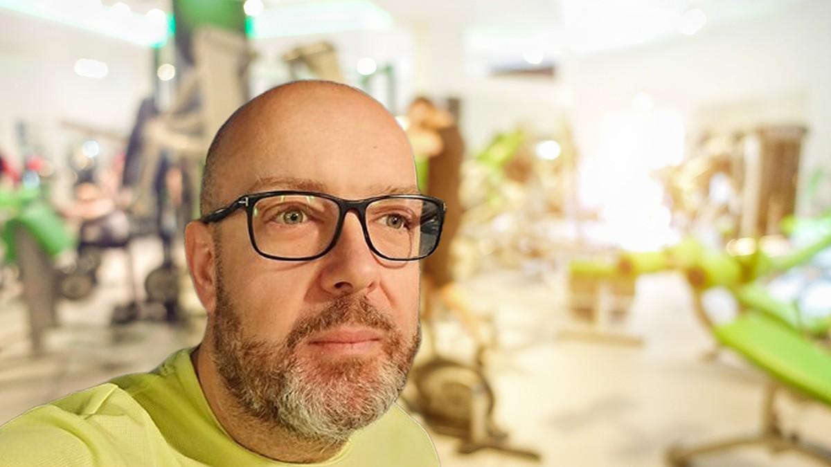 Un bărbat cu ochelari imracat intr-o bluza verde priveste. Este Radu Leca psiholog clinician, fost pacient cu obezitate, care a slabit 100 kg
