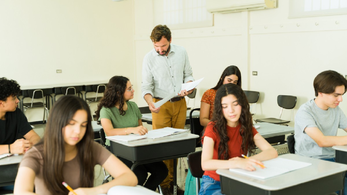 Profesor care supraveghează elevii de liceu în timp ce se concentrează pe examenele lor într-o clasă plină cu birouri și scaune