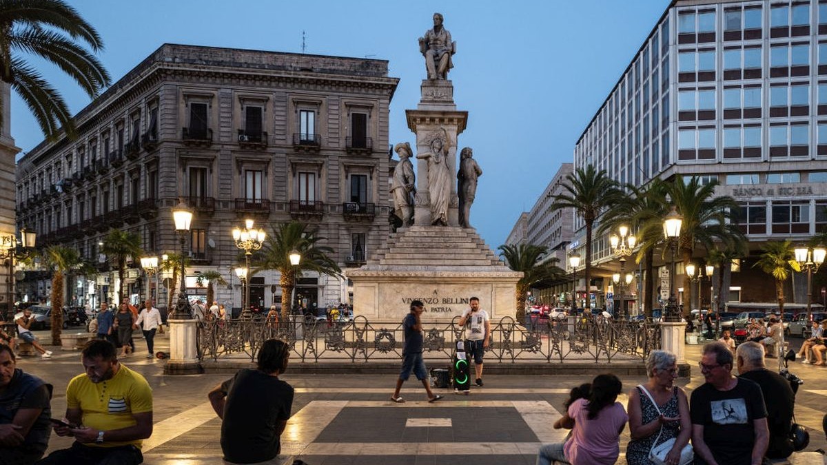 CATANIA, ITALY - JULY 28: A street singer sings under the statue of Catania's composer Vincenzo Bellini in Piazza Stesicoro, in front of some tourists sitting on the benches on July 28, 2023 in Catania, Italy. Italy is experiencing a severe heatwave, with 16 cities on red alert, including Palermo and Catania on the island of Sicily. (Photo by Fabrizio Villa/Getty Images)