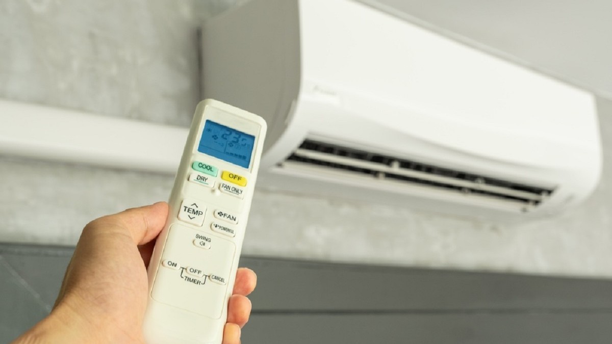 Imagine cu o mână de bărbat care ţine o televomandă în dreptul unui aparat de aer condiţionat