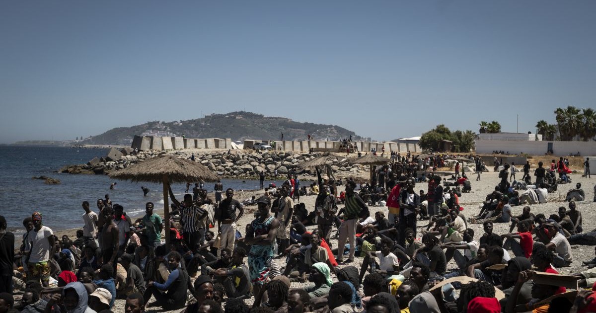 Migranți așteaptă pe plajă, lângă centrul CETI (Centrul de Ședere Temporară pentru Imigranți), la 2 august 2026, în Ceuta, Spania