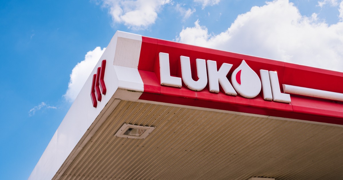 Logo-ul Lukoil cu alb, pe o suprafață roșie. În fundal, cerul este senin.