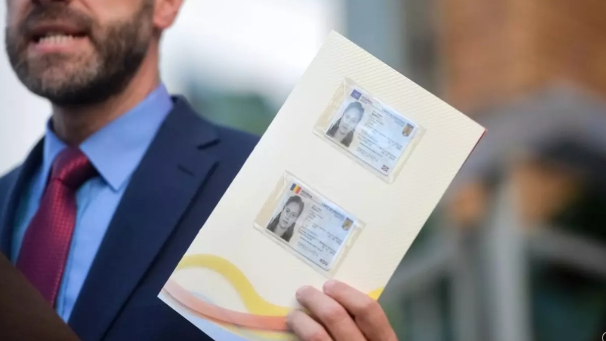În imagine este ilustrat un bărbat în costum care ține în mână o foaie pe care sunt două cărți de identitate electronice