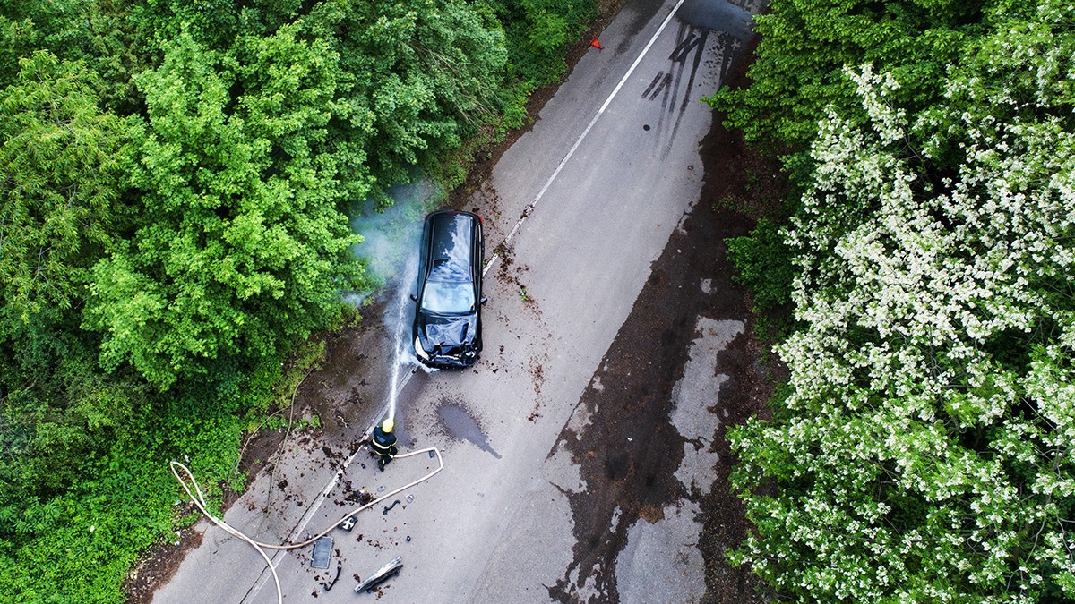 Pompieri care sting un incendiu al unei mașini accidentate