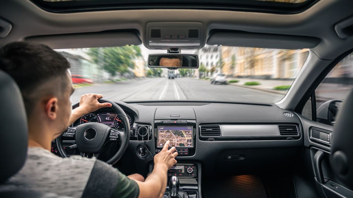 Un bărbat care este la volanul mașinii atinge ecranul unui sistem de navigație GPS