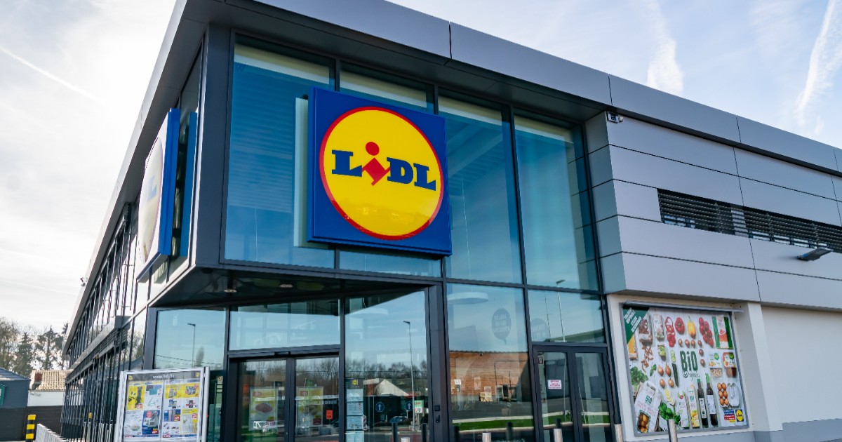Fațada unui magazin Lidl, pe care este amplasată sigla mare, circulară și multicoloră a retailerului, deasupra ușilor de la intrare.