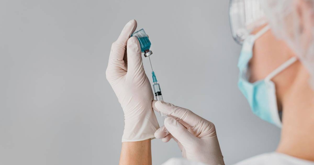 Un doctor în timp ce scoate serul pentru vaccin din fiolă, poartă mască și ochelari de protecție