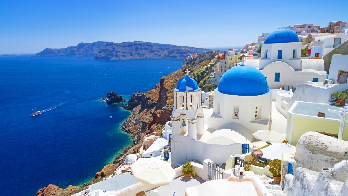 Peisaj din Santorini, clădiri albe construite pe stânci, privind spre apele albastre ale Mării Egee.