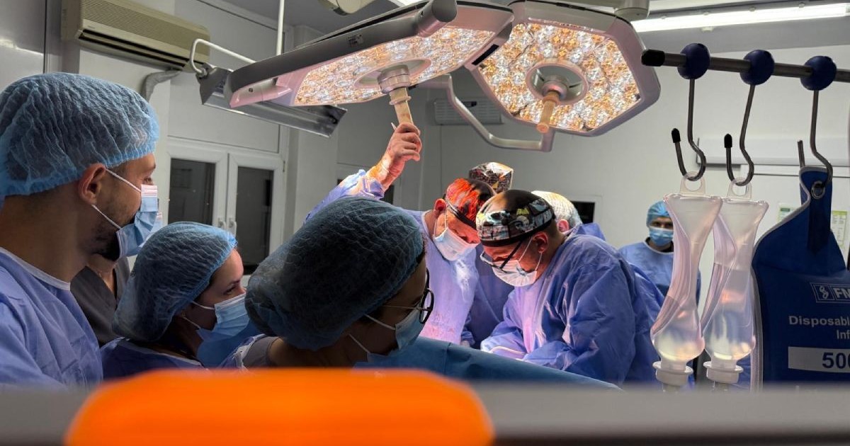 Medici echipați cu uniforme și măști, în timpul unei operații de transplant, într-o sală a unui spital, cu monitoare și lămpi,