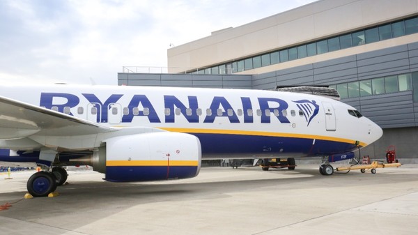 Un avion de pasageri al companiei Ryanair staționat pe pista unui aeroport, în fața unei clădiri moderne de terminal.