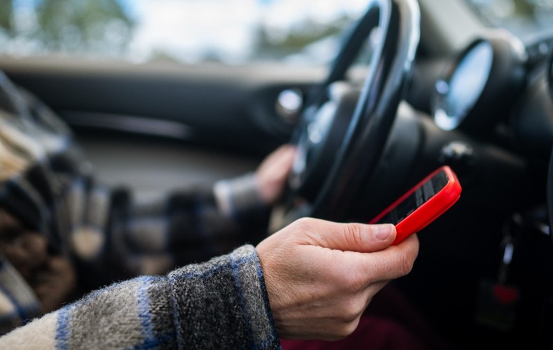 Un șofer la volan care conduce și ține un telefon în mâna dreaptă