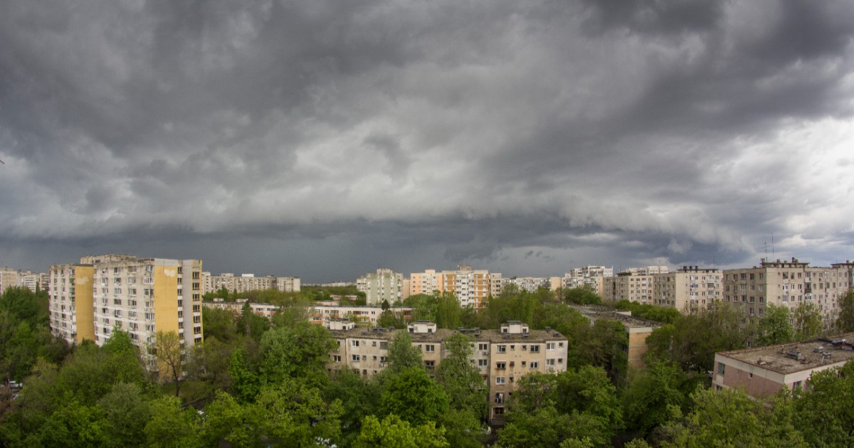 Blocuri de locuințe și copaci verzi, deasupra cărora se adună nori de furtună foarte întunecați și amenințători.