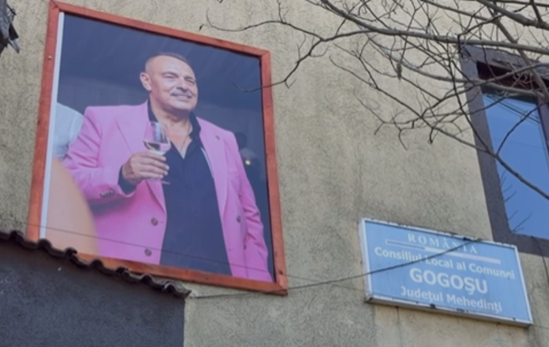 Primarul mort din satul Gogoșu „păzește” primăria cu un pahar de vin în mână, într-un sacou roz: cine a afișat tablourile vesele